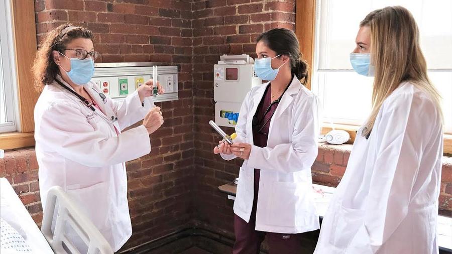 Nursing students listening in patient room to teacher.